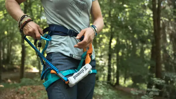 Person legt Klettersteigset an. Sicherungsgurt mit Karabiner und Seil im Wald.