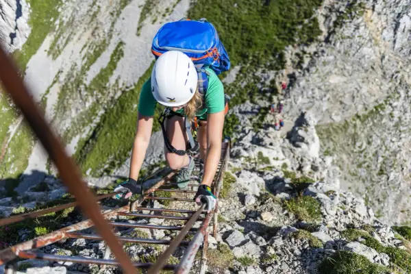 Bergsteigerin klettert eine Leiter hinauf. Die Klettersteige haben unterschiedliche Schwierigkeitsgrade, diese hier scheint mittelschwer zu sein.
