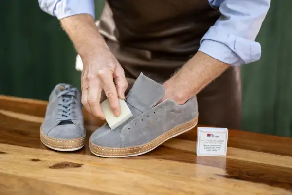 Mann reinigt graue Nubukleder-Sneaker mit einem speziellen Radierer.