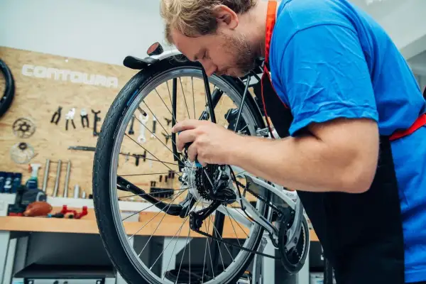 Ein Mann mit Bart im blauen T-Shirt und schwarzer Schürze arbeitet konzentriert am Fahrrad. Er wechselt das Fahrrad Schaltwerk.