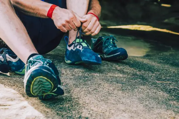 Hände schnüren blaue Kletterschuhe, bereit für den nächsten Aufstieg. Die Füße sind für das Klettern vorbereitet, um die Felsen zu meistern.