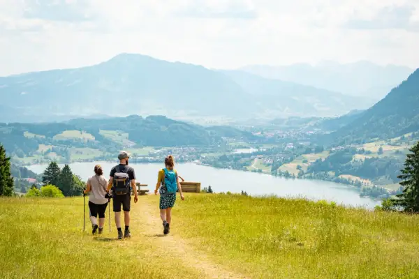 Drei Personen genießen eine leichte Wanderung mit Blick auf einen See und Berge.