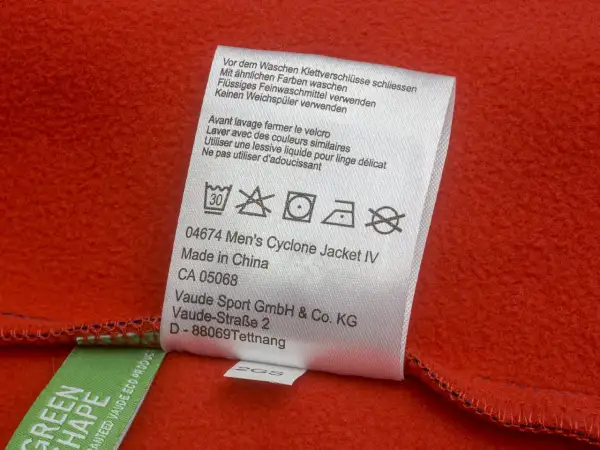 Pflegeetikett einer roten Softshell-Jacke. Hinweise zur Wäsche, z.B. 30°C, kein Trockner.